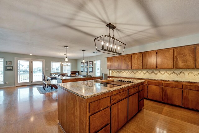 1327 Tiki Dr, Tiki Island, TX 77554 - kitchen with a kitchen island, brown cabinetry, wood finished floors, decorative backsplash, and light stone counters
