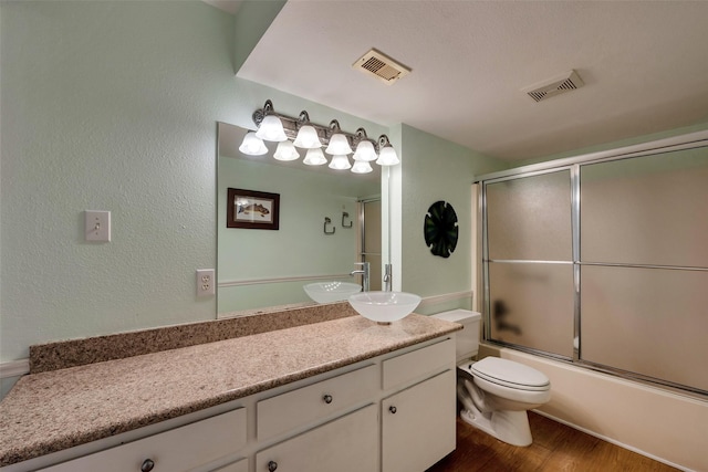 1327 Tiki Dr, Tiki Island, TX 77554 - full bathroom with vanity, toilet, wood finished floors, shower / bath combination with glass door, and a textured wall
