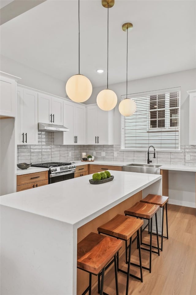 3516 Piney Woods Dr, Houston, TX 77018 - kitchen with under cabinet range hood, a sink, stainless steel gas range oven, light wood-type flooring, and light countertops