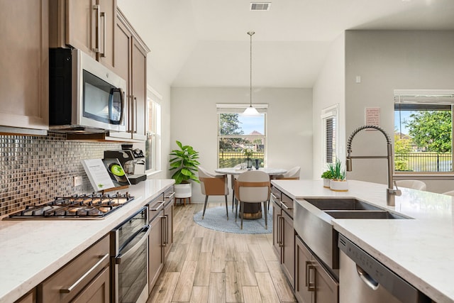 24743 Levante Dr, Richmond, TX 77406 - kitchen with stainless steel appliances, a sink, light wood finished floors, pendant lighting, and backsplash