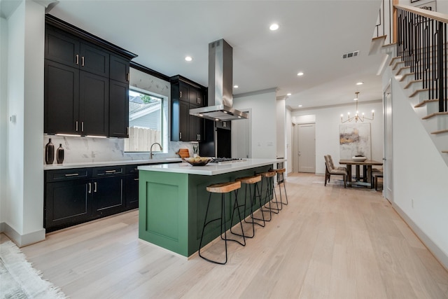 1724 Ridgewood St, Houston, TX 77006 - kitchen with island exhaust hood, light wood-style floors, light countertops, dark cabinetry, and decorative backsplash
