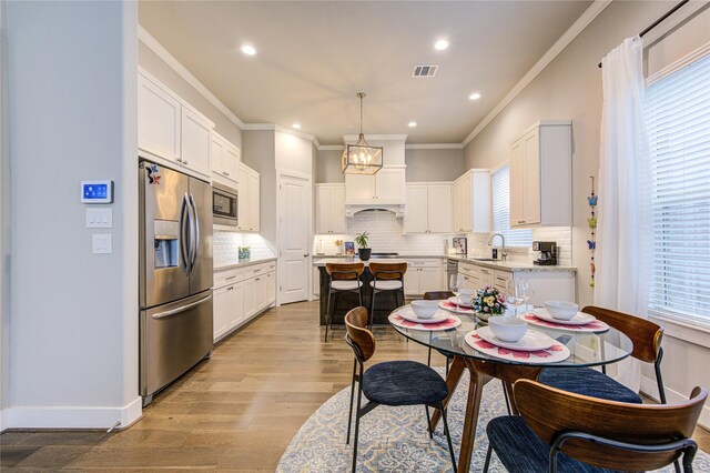 10918 Brookeshire Chase Ln, Houston, TX 77043 - kitchen featuring appliances with stainless steel finishes, a sink, crown molding, white cabinetry, and light wood-style flooring