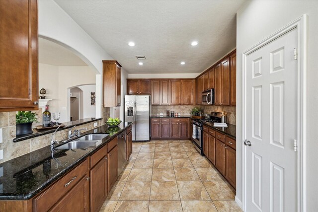 13303 Bomoseen Lake Rd, Houston, TX 77044 - kitchen featuring appliances with stainless steel finishes, a sink, decorative backsplash, arched walkways, and dark stone counters