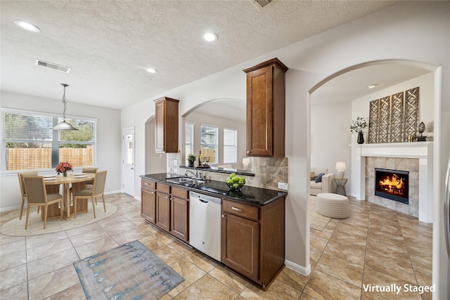 13303 Bomoseen Lake Rd, Houston, TX 77044 - kitchen with stainless steel dishwasher, a sink, arched walkways, a tiled fireplace, and a textured ceiling