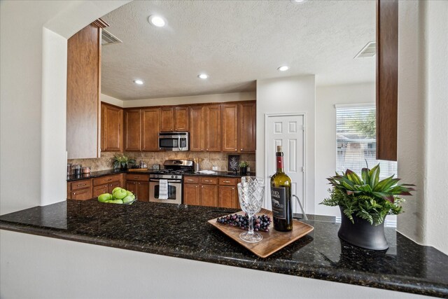 13303 Bomoseen Lake Rd, Houston, TX 77044 - kitchen featuring stainless steel appliances, decorative backsplash, brown cabinets, arched walkways, and a textured ceiling