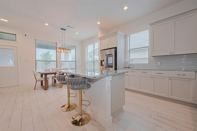 21307 Metallic Blue Dr, Cypress, TX 77433 - kitchen with stainless steel fridge, light stone countertops, a center island, a kitchen bar, and recessed lighting