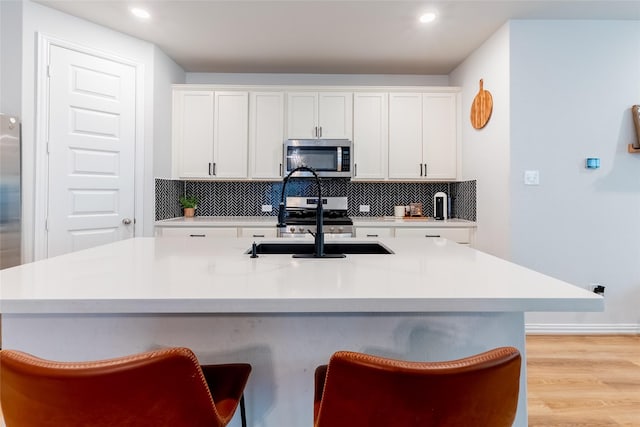 16935 Lagos Ln, Crosby, TX 77532 - kitchen with appliances with stainless steel finishes, decorative backsplash, light wood-style floors, a breakfast bar area, and white cabinets