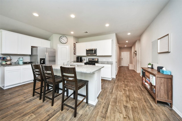 14133 Sharktooth Hill Ln, Conroe, TX 77384 - kitchen with stainless steel appliances, dark wood finished floors, light stone countertops, white cabinets, and a center island with sink