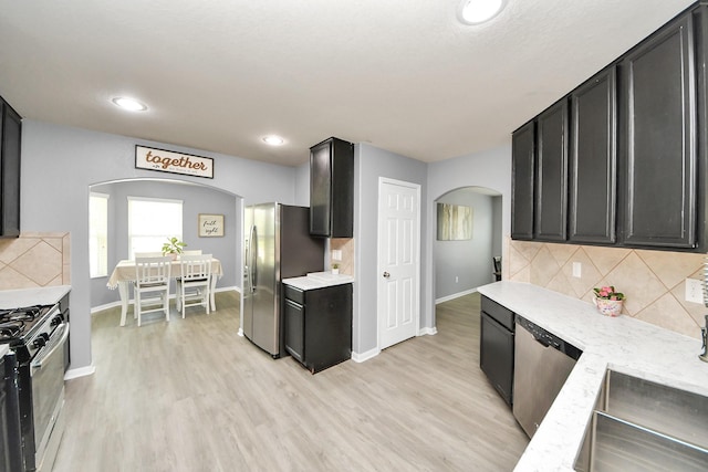 15543 Sheldon Ridge Way, Houston, TX 77044 - kitchen with arched walkways, appliances with stainless steel finishes, decorative backsplash, light wood-style floors, and baseboards