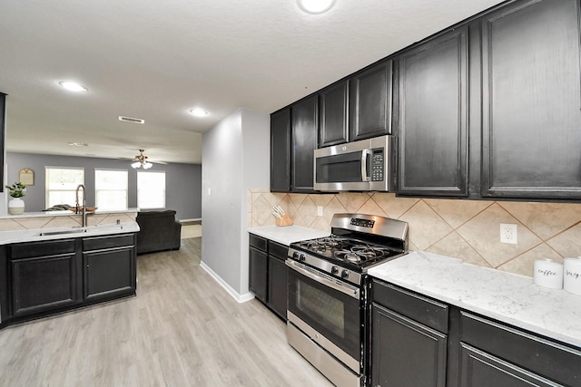 15543 Sheldon Ridge Way, Houston, TX 77044 - kitchen featuring appliances with stainless steel finishes, a sink, dark cabinets, light wood-style flooring, and decorative backsplash