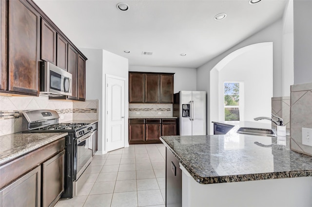 30510 Legend Oaks Ct, Magnolia, TX 77355 - kitchen featuring appliances with stainless steel finishes, a sink, arched walkways, dark stone counters, and dark brown cabinetry