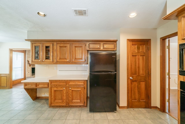 6914 Coral Ridge Rd, Houston, TX 77069 - kitchen featuring freestanding refrigerator, light countertops, brown cabinets, glass insert cabinets, and light tile patterned floors