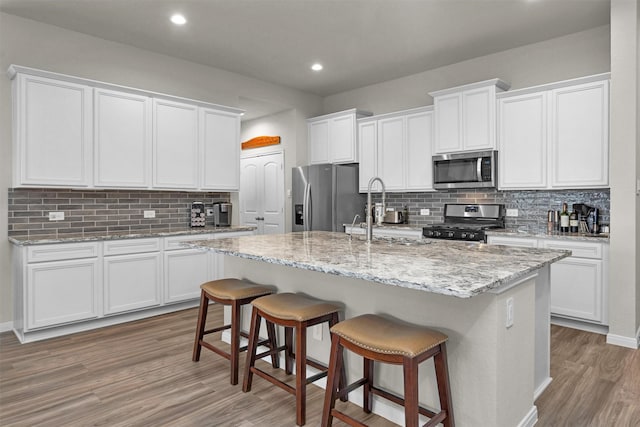 1217 Antelope Passing Dr, Montgomery, TX 77316 - kitchen with stainless steel appliances, light wood finished floors, tasteful backsplash, a kitchen breakfast bar, and an island with sink