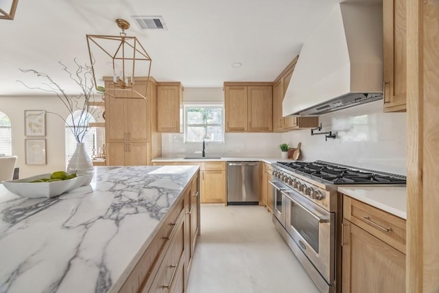2906 Riata Ln, Houston, TX 77043 - kitchen with appliances with stainless steel finishes, wall chimney range hood, a sink, light stone counters, and hanging light fixtures