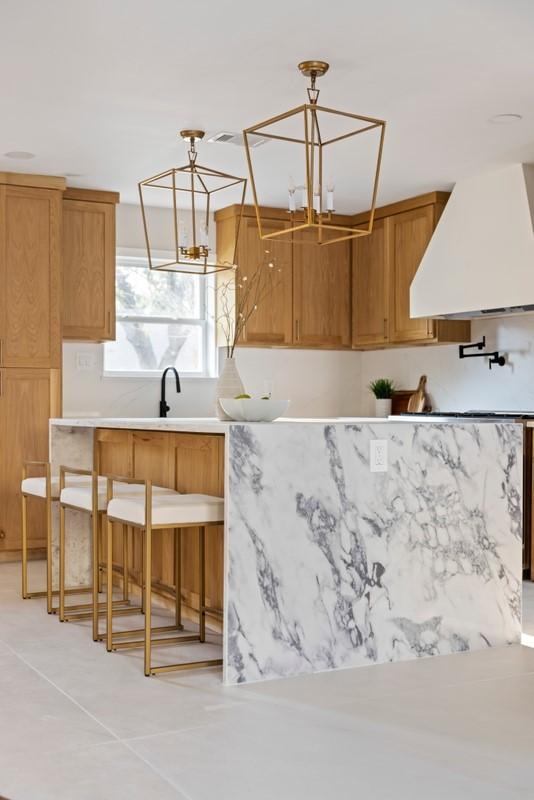 2906 Riata Ln, Houston, TX 77043 - kitchen with custom range hood, light countertops, hanging light fixtures, a breakfast bar area, and brown cabinetry