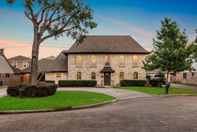 2906 Riata Ln, Houston, TX 77043 - french country style house with a shingled roof, a front yard, curved driveway, central air condition unit, and brick siding