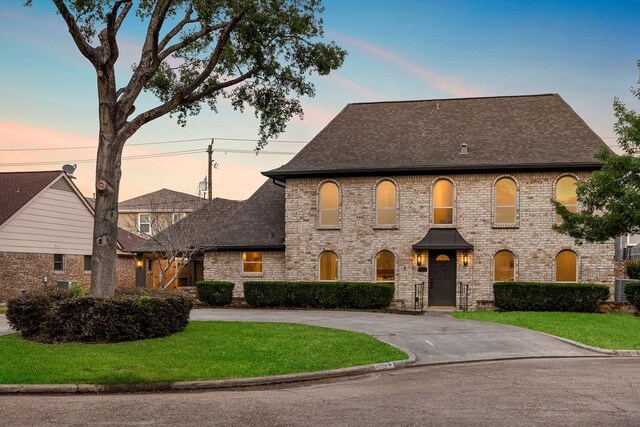 2906 Riata Ln, Houston, TX 77043 - french country style house featuring a shingled roof, a yard, brick siding, and curved driveway