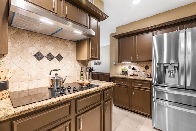 7 E Torch Pine Cir, The Woodlands, TX 77381 - kitchen with stainless steel refrigerator with ice dispenser, under cabinet range hood, tasteful backsplash, black electric cooktop, and light stone counters