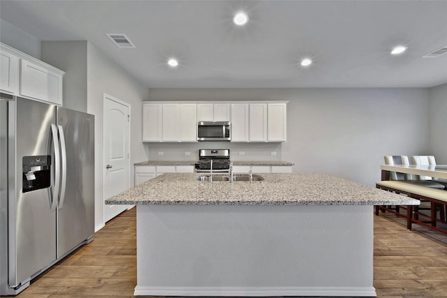 13854 Rock Island Trl, Conroe, TX 77384 - kitchen with stainless steel appliances, a sink, white cabinets, wood finished floors, and a kitchen island with sink