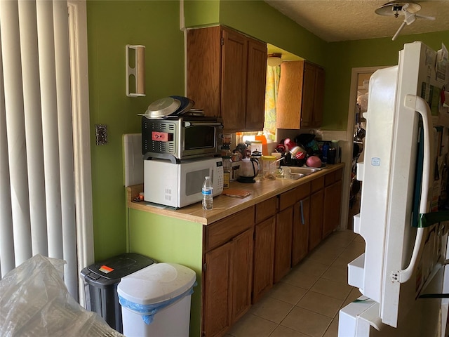 4403 Trailwood Dr, San Antonio, TX 78228 - kitchen featuring white appliances, light countertops, light tile patterned flooring, brown cabinetry, and a sink