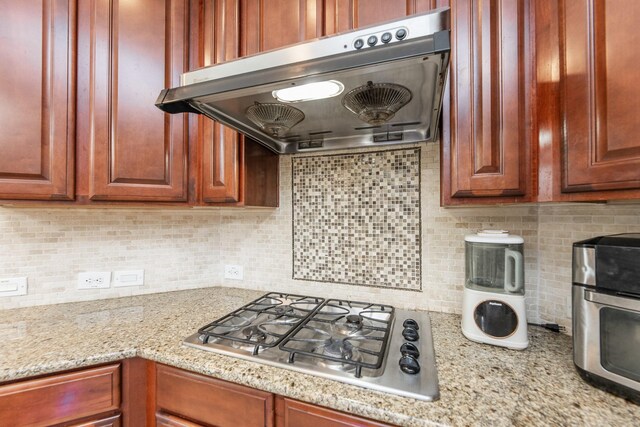 13422 Great Creek Dr, Pearland, TX 77584 - kitchen with under cabinet range hood, stainless steel gas stovetop, backsplash, and light stone countertops