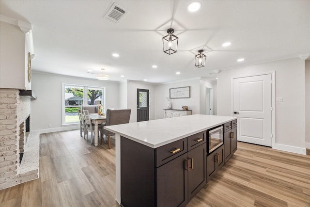 2007 Ottawa Ln, Houston, TX 77043 - kitchen featuring ornamental molding, recessed lighting, light wood-style flooring, a kitchen island, and a brick fireplace