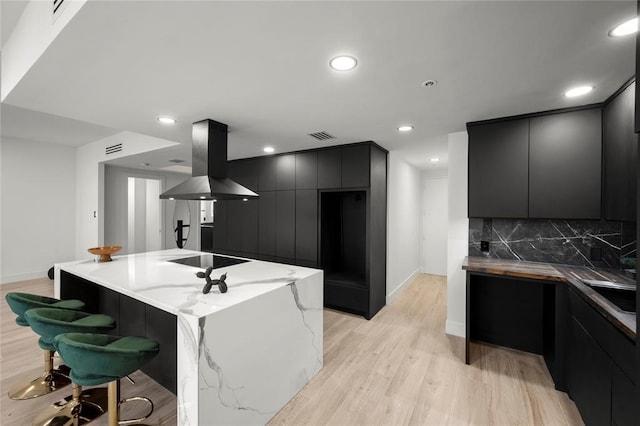 5555 Del Monte Dr Unit 103, Houston, TX 77056 - kitchen featuring modern cabinets, island range hood, light wood-style floors, black electric cooktop, and tasteful backsplash
