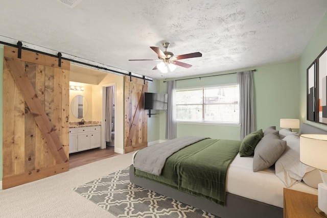 14922 Sandy Creek Dr, Houston, TX 77070 - carpeted bedroom featuring a barn door, a textured ceiling, connected bathroom, a ceiling fan, and a sink