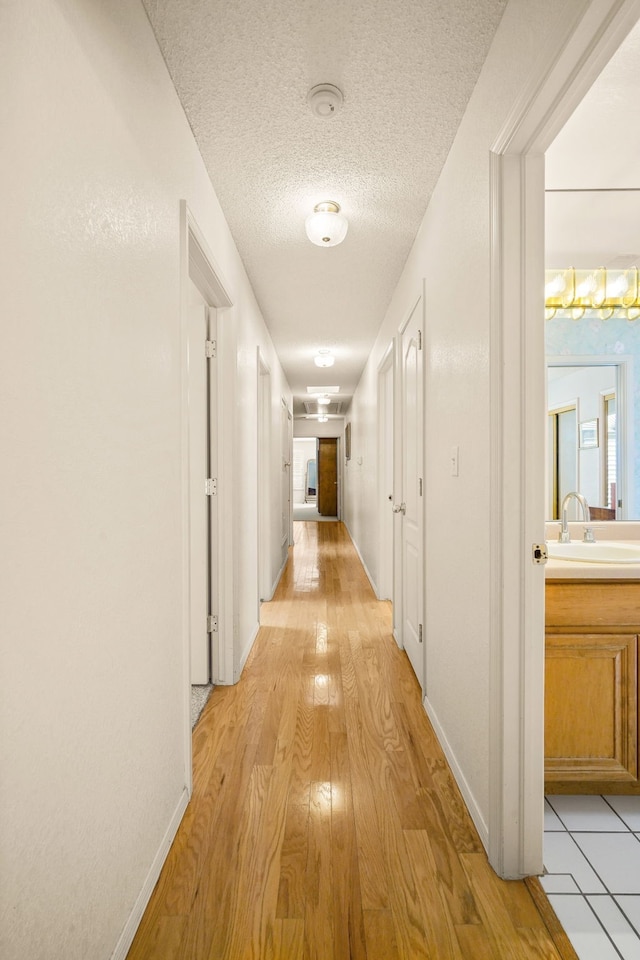6574 Eagle Ridge Dr, El Paso, TX 79912 - hallway with a sink, light wood-type flooring, baseboards, and a textured ceiling