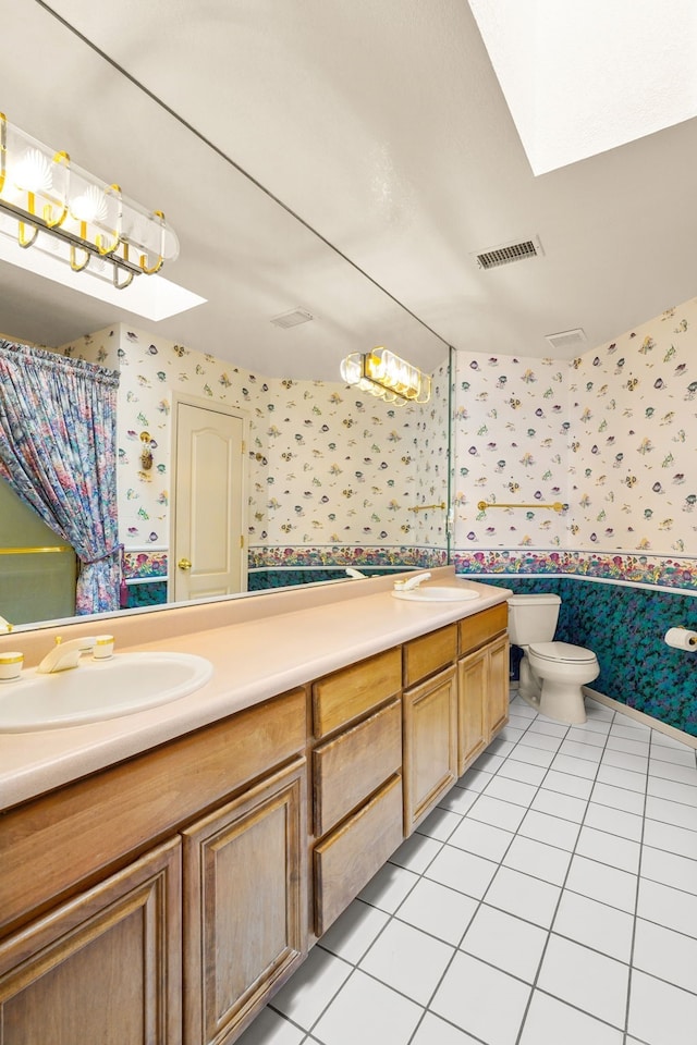 6574 Eagle Ridge Dr, El Paso, TX 79912 - full bathroom featuring wallpapered walls, a skylight, double vanity, tile patterned flooring, and toilet