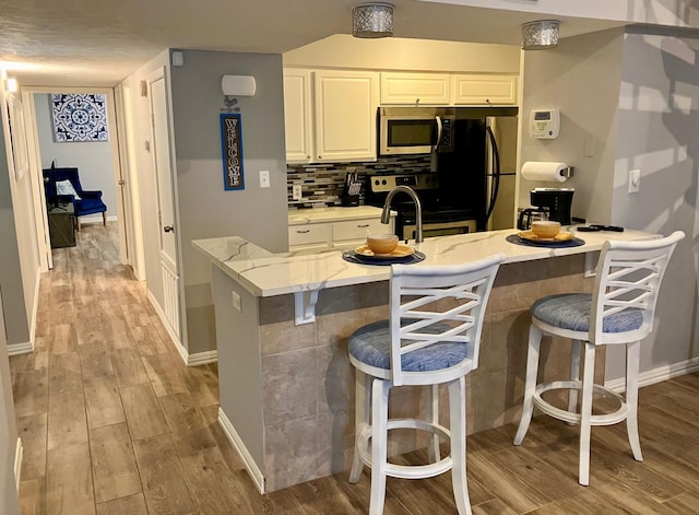 12500 Melville Dr Unit 233D, Montgomery, TX 77356 - kitchen with stainless steel appliances, light wood-type flooring, a breakfast bar area, light stone countertops, and white cabinetry