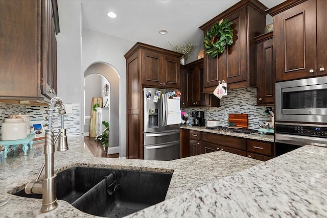 231 N Waterstone Dr, Montgomery, TX 77356 - kitchen featuring stainless steel appliances, a sink, backsplash, arched walkways, and light stone countertops