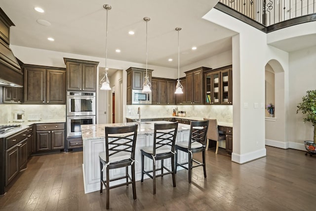 9810 Mount Whitney, Missouri City, TX 77459 - kitchen with stainless steel appliances, dark brown cabinets, a kitchen island with sink, backsplash, and dark wood-style floors