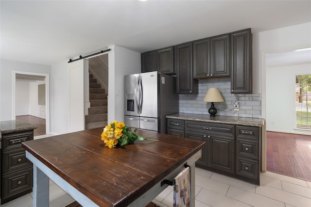215 Whispering Oaks Dr, Taylor Lake Village, TX 77586 - kitchen featuring stainless steel fridge, a barn door, tasteful backsplash, stone countertops, and light tile patterned floors