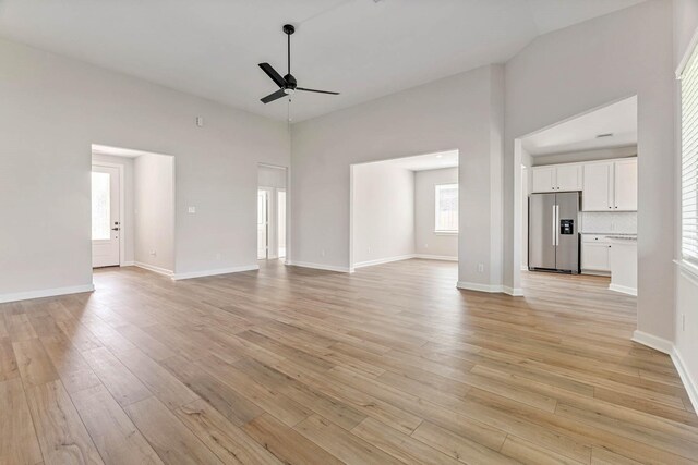 1927 June Lake Ln, Iowa Colony, TX 77583 - unfurnished living room with a ceiling fan, light wood-style flooring, a towering ceiling, and baseboards