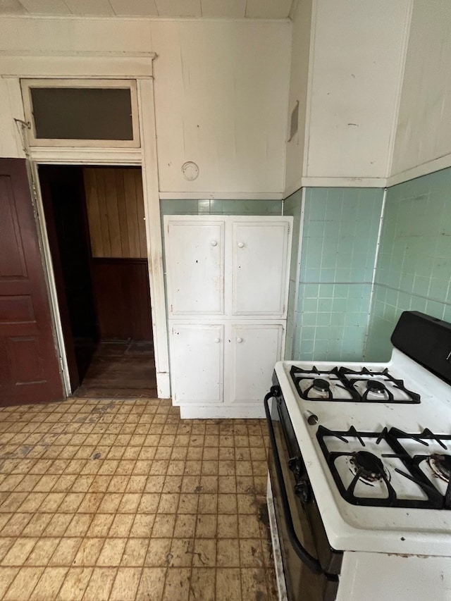 614 18th St, Galveston, TX 77550 - kitchen with white gas stove, tile walls, a wainscoted wall, and white cabinetry