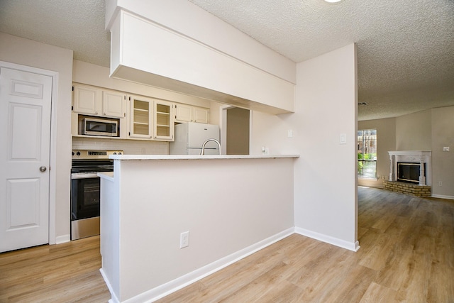 5001 Lamonte Ln Unit 14, Houston, TX 77092 - kitchen featuring stainless steel appliances, a textured ceiling, light wood-style flooring, glass insert cabinets, and a peninsula