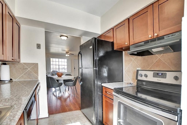 9003 Gaylord St Unit 12, Houston, TX 77024 - kitchen featuring stainless steel appliances, under cabinet range hood, a ceiling fan, brown cabinetry, and backsplash