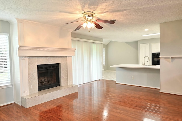 3114 Hollow Creek Ct, Houston, TX 77082 - unfurnished living room featuring a sink, ceiling fan, wood finished floors, a tiled fireplace, and a textured ceiling