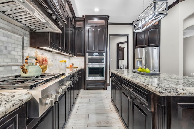 5912 T St, Katy, TX 77493 - kitchen featuring appliances with stainless steel finishes, wall chimney range hood, tasteful backsplash, light stone countertops, and arched walkways