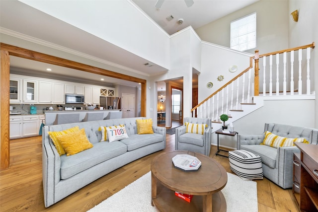 1538 Bevis St, Houston, TX 77008 - living room featuring light wood-style flooring, ornamental molding, a towering ceiling, stairs, and ceiling fan