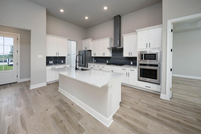 10618 Sutter Creek Dr, Iowa Colony, TX 77583 - kitchen featuring appliances with stainless steel finishes, wall chimney range hood, a sink, an island with sink, and tasteful backsplash