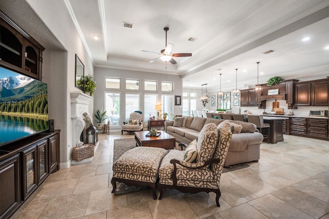 9811 Orchid Cove Ct, Cypress, TX 77433 - living room featuring ceiling fan, a fireplace, a tray ceiling, crown molding, and stone tile flooring