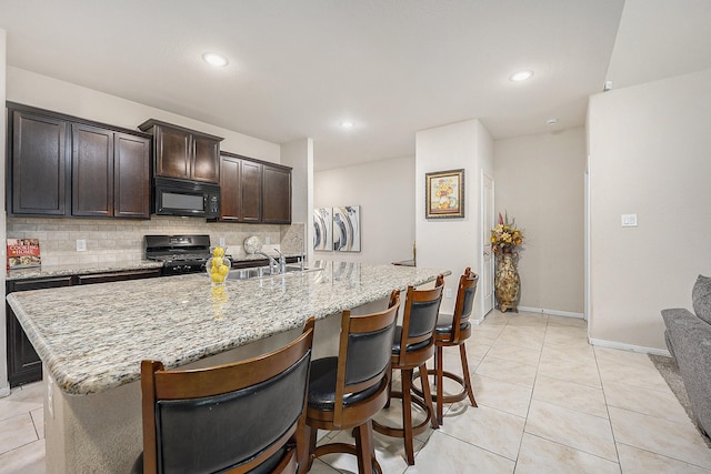 9407 Mineral Rock Ln, Richmond, TX 77407 - kitchen featuring black microwave, stove, tasteful backsplash, an island with sink, and dark brown cabinetry