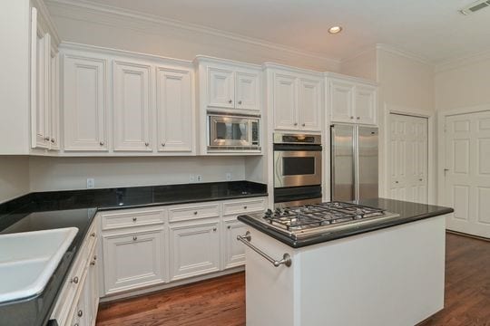 5422 Gibson St Unit A, Houston, TX 77007 - kitchen with appliances with stainless steel finishes, white cabinetry, dark countertops, crown molding, and dark wood finished floors