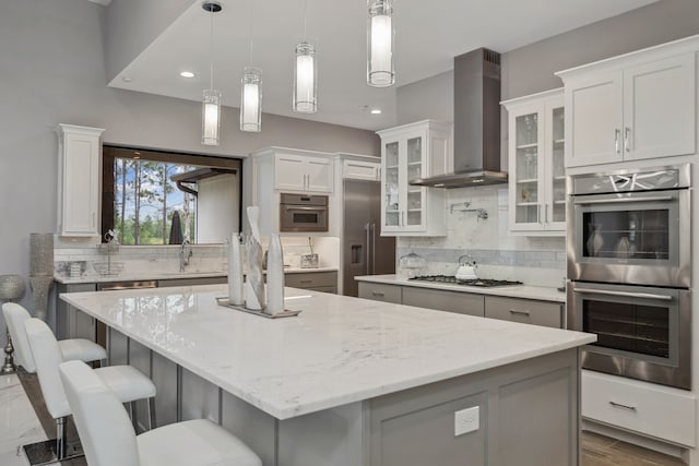 27457 S Lazy Meadow Way, Spring, TX 77386 - kitchen with wall chimney exhaust hood, stainless steel double oven, gas stovetop, a kitchen island, and tasteful backsplash