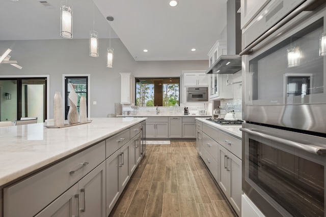 27457 S Lazy Meadow Way, Spring, TX 77386 - kitchen featuring stainless steel double oven, range hood, backsplash, hanging light fixtures, and light wood-style flooring