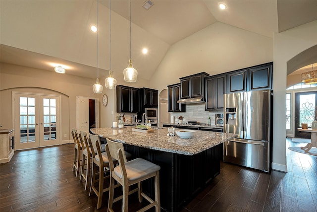 2625 Blooming Field Ln, Conroe, TX 77385 - kitchen featuring appliances with stainless steel finishes, arched walkways, light stone counters, dark cabinetry, and dark wood finished floors