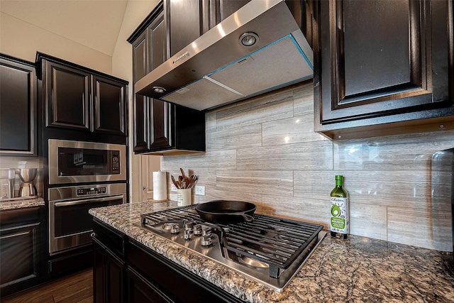 2625 Blooming Field Ln, Conroe, TX 77385 - kitchen with range hood, appliances with stainless steel finishes, decorative backsplash, dark stone countertops, and dark wood-style flooring