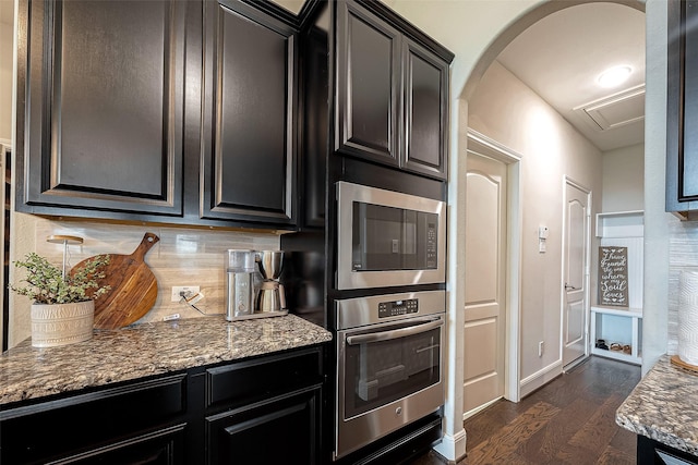 2625 Blooming Field Ln, Conroe, TX 77385 - kitchen with appliances with stainless steel finishes, dark wood-style floors, decorative backsplash, arched walkways, and dark stone countertops